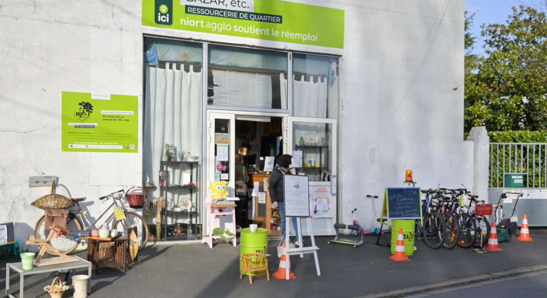 Façade de la ressourcerie Bazar, etc. avec meubles, vélos et objets de seconde main exposés devant l'entrée