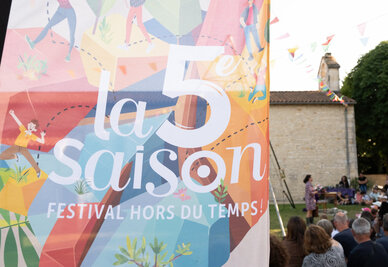 Affiche « Festival hors du temps » au premier plan, public nombreux assistant à un spectacle de plein air dans un cadre villageois
