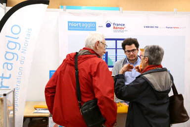 Stand Niort Agglo / France Rénov' lors d'un salon : un conseiller renseigne deux visiteurs sur leurs projets de rénovation
