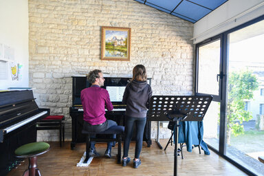 Cours de piano à l'antenne de Chauray : un professeur au clavier accompagne un élève debout face à la partition