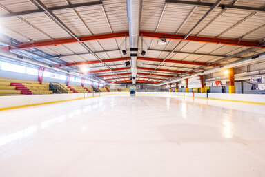 Piste de glace lisse et brillante fraîchement surfacée, tribunes vides et charpente métallique rouge de la patinoire en arrière-plan